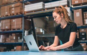 A person standing in a warehouse and working on a laptop