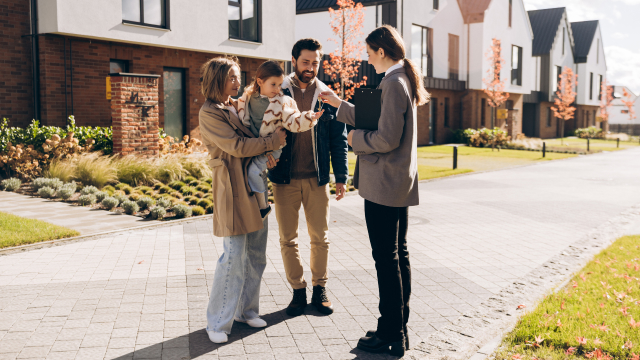 Real estate agent handing house keys to a family outside a residential neighborhood