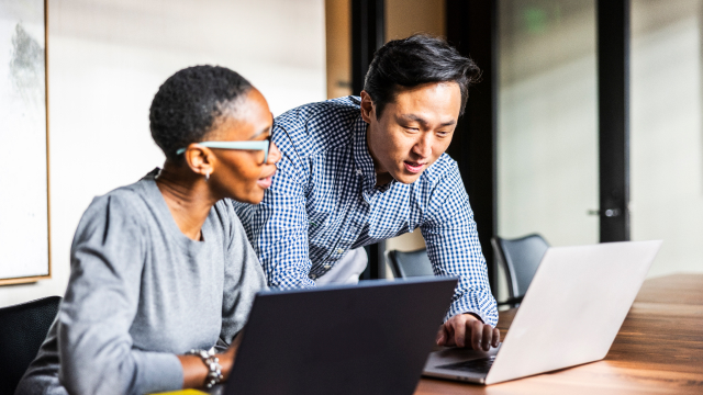 Two colleagues reviewing documents on a laptop