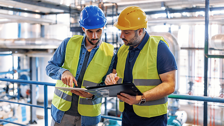Two men in hard hats in industrial environment looking at paperwork