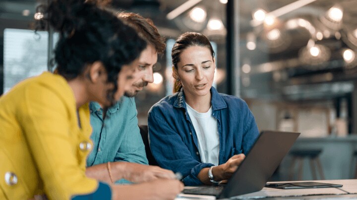 Three people working together on a laptop in an office.